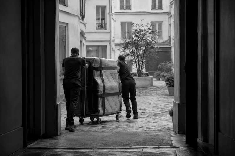 Piano droit emballé poussé sur un chariot dans une cour pavée parisienne