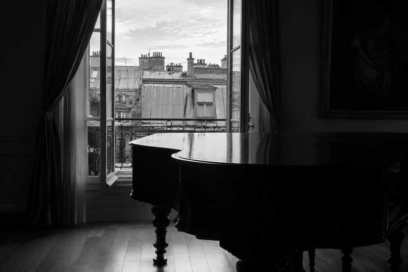 Piano à queue devant une fenêtre ouverte sur les toits de zinc parisiens