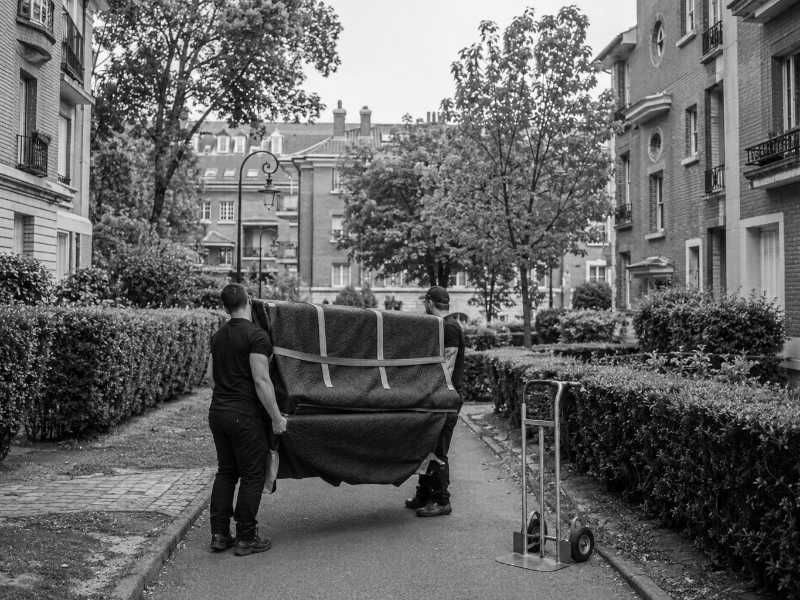 Portage d’un piano droit dans une allée de cité-jardin à Châtenay-Malabry (92)