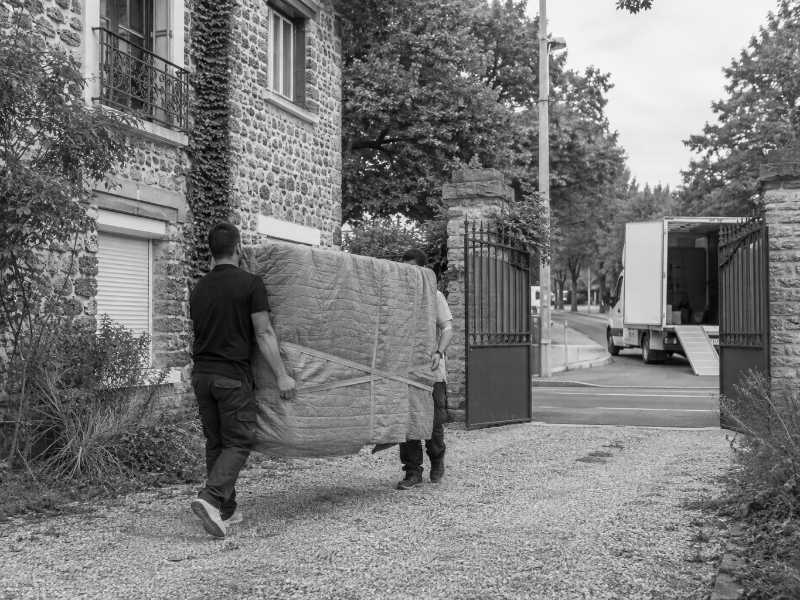 Portage d’un piano droit emballé dans l’allée gravillonnée d’une maison à Marnes-la-Coquette (92)