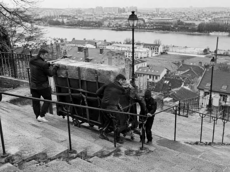 Descente d’un piano droit sanglé le long d’un escalier public à Saint-Cloud (92)