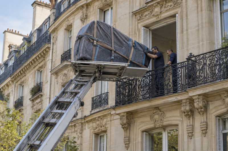 Piano à queue emballé hissé par un monte-meubles jusqu'au balcon d'un immeuble haussmannien, Paris 1er