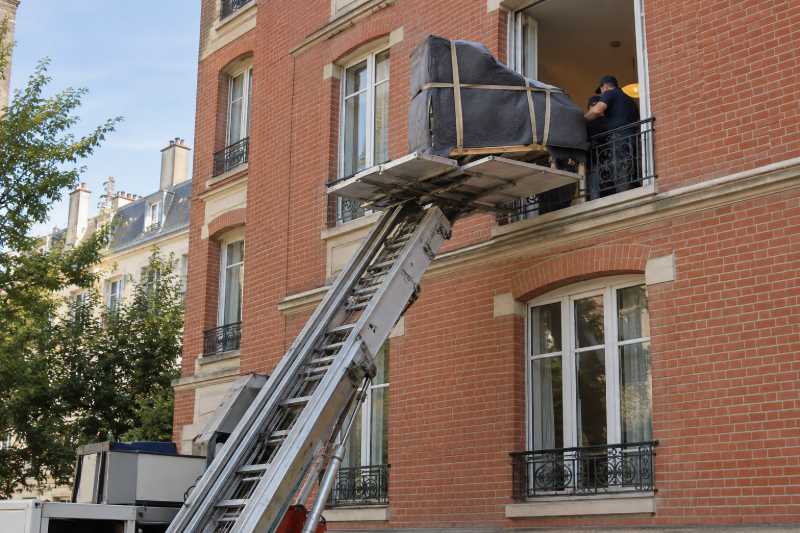 Piano quart-de-queue emballé hissé au monte-meubles vers la baie d'un immeuble en brique, Lieusaint