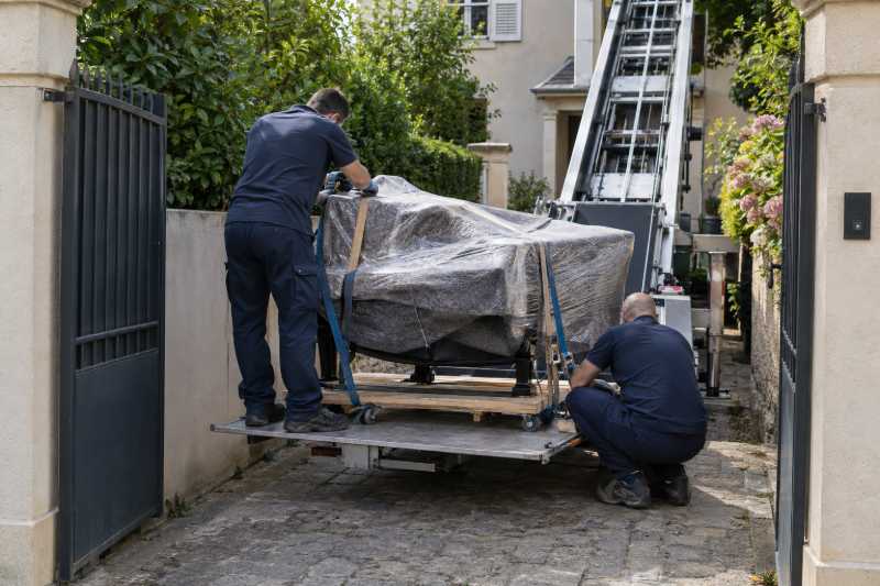 Déménageurs sanglant un piano à queue emballé sur le plateau d'un monte-meubles dans une allée