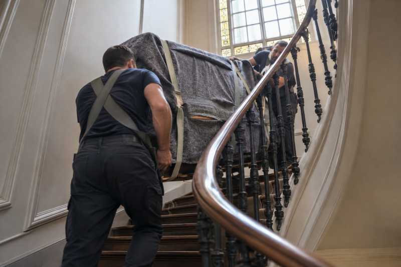 Deux déménageurs au harnais négociant un palier d'escalier tournant avec un piano droit, Avon