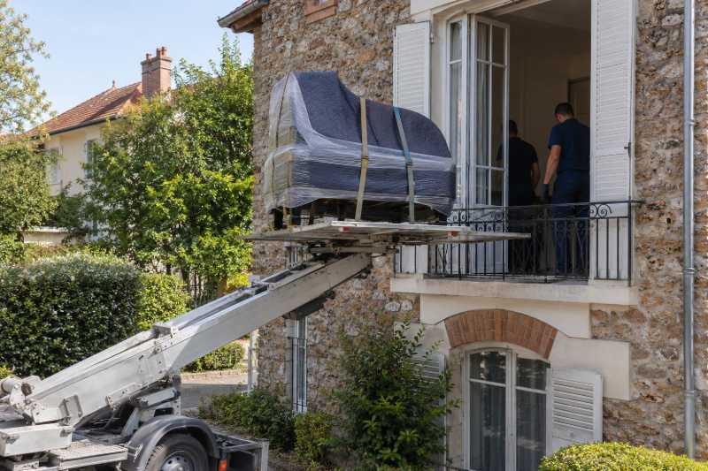 Piano demi-queue emballé arrivant par monte-meubles à la porte-fenêtre d'une maison en meulière, Paris 20e