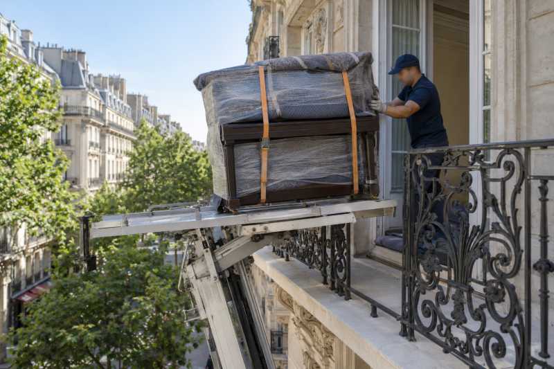 Piano droit emballé hissé au monte-meubles jusqu'à un balcon haussmannien
