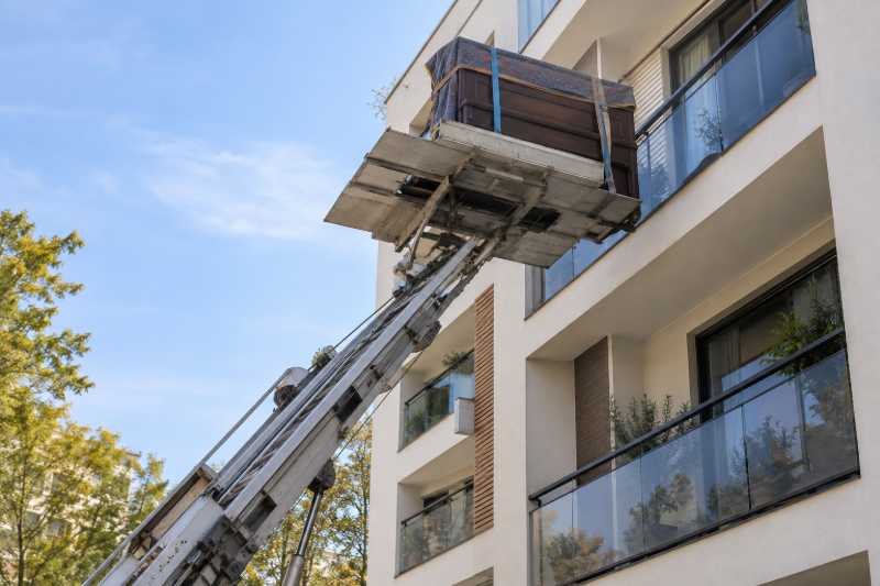 Piano droit emballé hissé par un monte-meubles le long d'une résidence moderne, Paris 7e